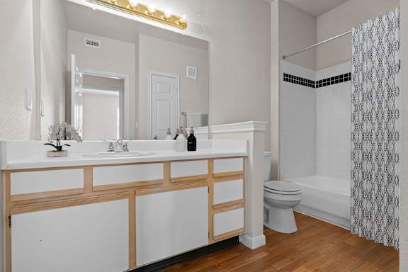 A large bathroom with white oak cabinets, a large vanity mirror, lots of counterspace, and a tub shower combo.