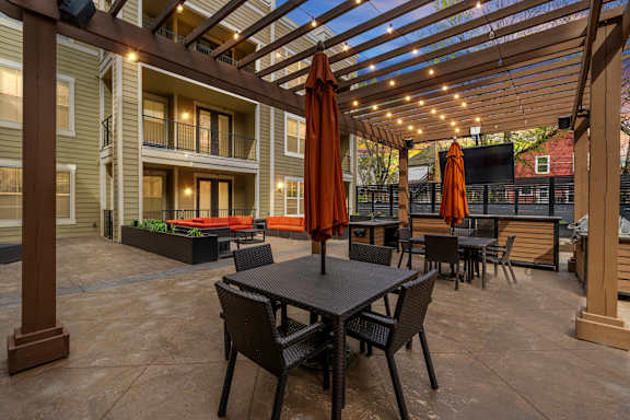 Outdoor lounge at West 39th Street Apartments with pergola, string lights, dining tables, and mounted TV at West 39th Street Apartments, Missouri, 64111