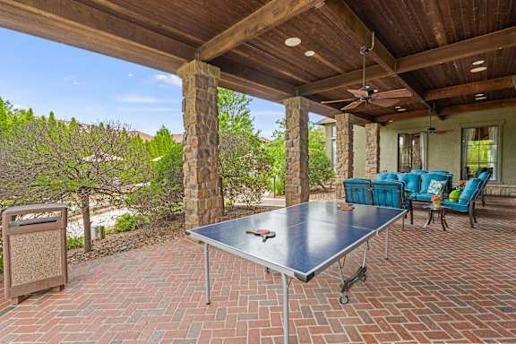 A table is on a patio with a blue couch and a fan.