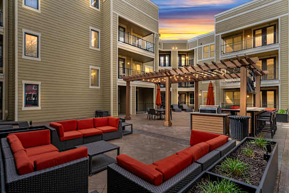 Sunset view of the outdoor courtyard at West 39th Street Apartments with red cushioned lounge seating, pergola, and grilling station at West 39th Street Apartments, Kansas City, 64111