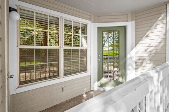 A private balcony with white railing, large windows, and a green door.