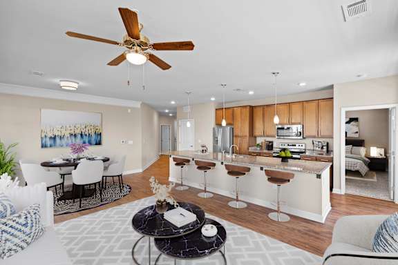 A living room with a ceiling fan, hardwood floors, crown molding and bartop dining.