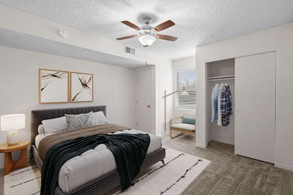 A bedroom with a bed, a ceiling fan, and a wardrobe.