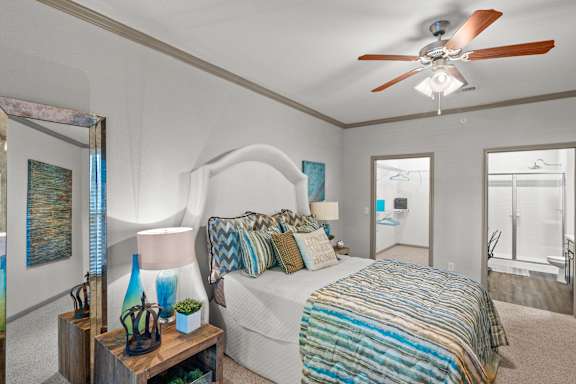 A bedroom with a bed, a ceiling fan, and a nightstand with a lamp and vases.