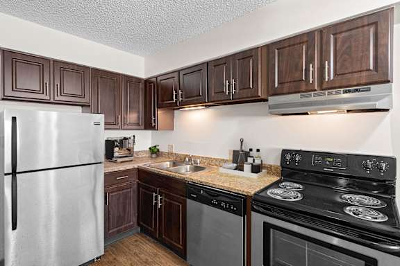 A kitchen with stainless steel appliances, dark wood cabinets, and granite countertops.