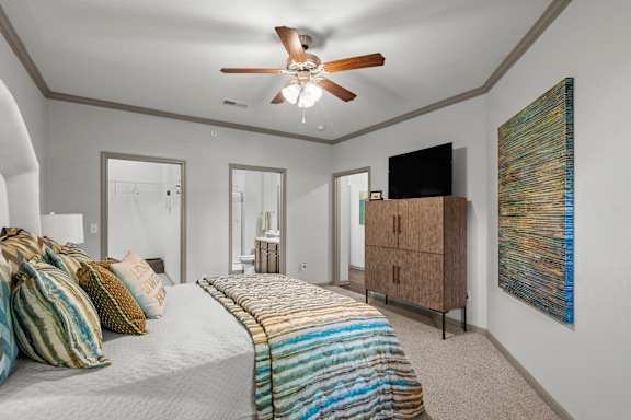 A bedroom with a bed, a ceiling fan, and a painting on the wall.
