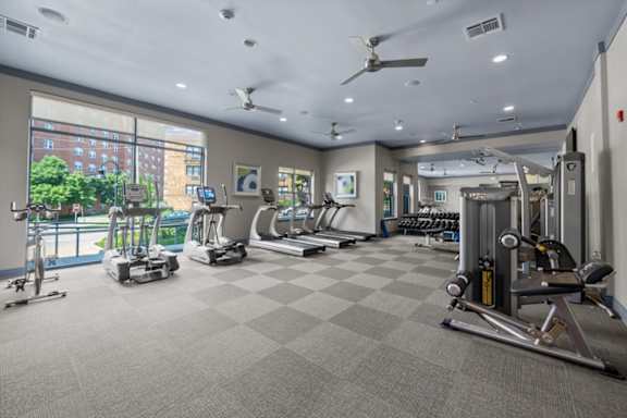 A spacious gym with a variety of equipment and a view of a cityscape outside the window.