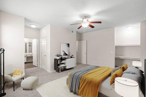 A large bedroom with a built in shelf, a ceiling fan, and an attached master bathroom.