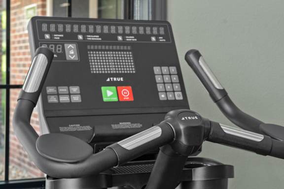 A close up of a True bike workout machine with a digital screen and handlebars.