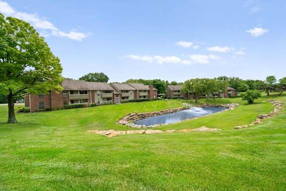 A small pond in the middle of a grassy area with a building in the background. at Coventry Oaks Apartments, Kansas