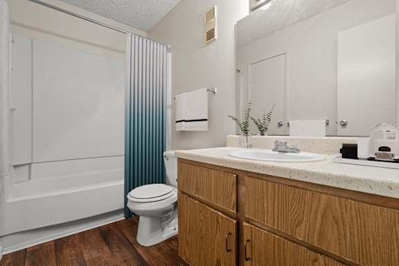 A bathroom with wooden storage cabinets, a large vanity mirror, lots of counter space, a toilet, and a tub shower combo.