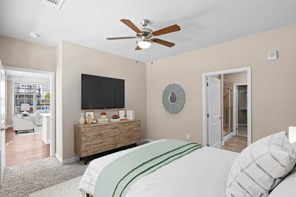 A bedroom with a ceiling fan, carpeting, and an attached master bathroom.