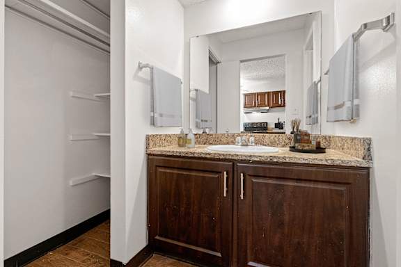 A bathroom with granite countertops, storage cabinets, a large vanity mirror, towel racks, and an open linen closet with wire rack shelves.