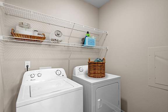 A full-size washer & dryer included inside a laundry room with a wire rack shelf.
