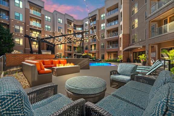 A modern outdoor seating area with wicker chairs and tables is set up in front of apartment buildings.