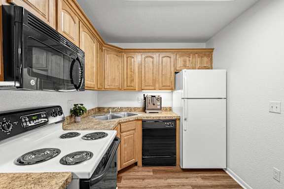 A kitchen with granite countertops, white and black appliances, oak cabinets and a dishwasher.