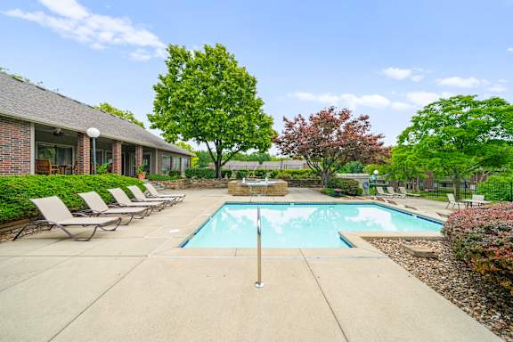 A pool surrounded by trees and chairs in front of a house. at Coventry Oaks Apartments, Overland Park 66214