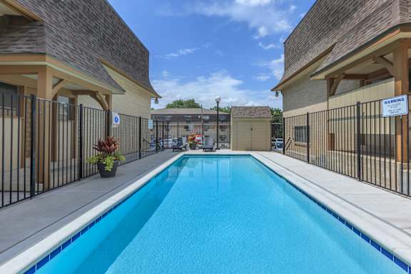 A swimming pool surrounded by a black fence and a warning sign. at Malvern Hill Apartment Homes, Kansas