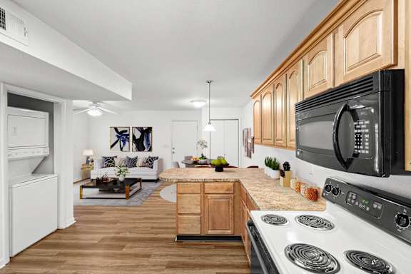 A kitchen with washer and dryer, upgraded lighting, black & white appliances, and oak cabinets.