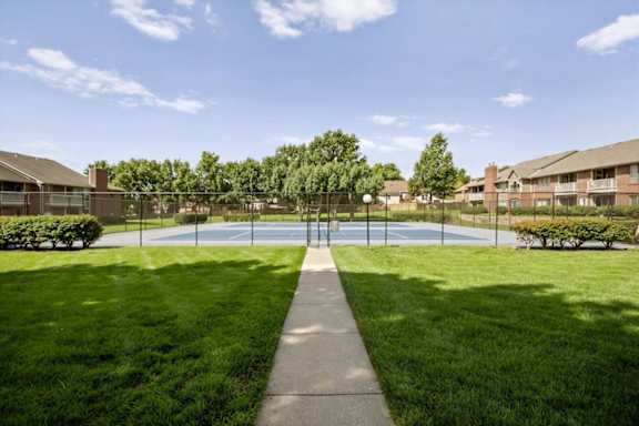 Walkway leading to fenced tennis courts surrounded by open green space and apartment homes.