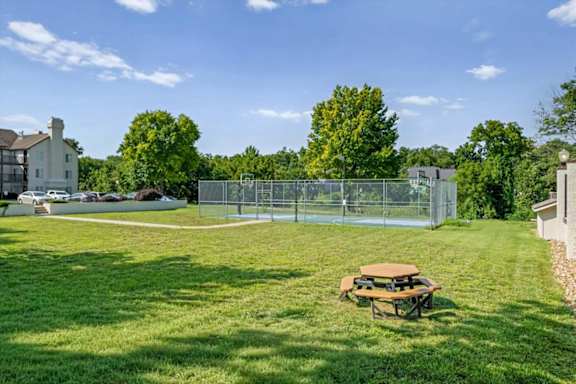 Outdoor basketball court surrounded by green lawn and mature trees at Millcreek Woods Apartment Homes.
