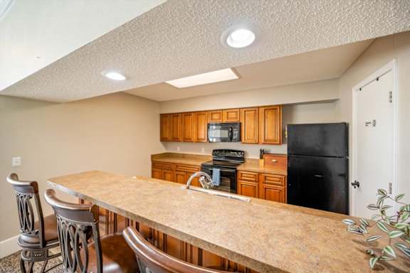 Clubhouse kitchen featuring wood cabinetry, black appliances, and breakfast bar seating.