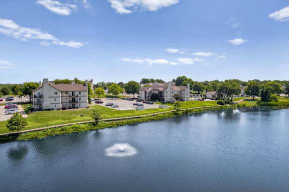 Decorative fountain in the community lake with apartment homes and mature trees nearby.