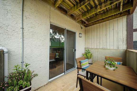 Spacious covered patio with outdoor seating, wood ceiling accents, and access to the apartment interior.