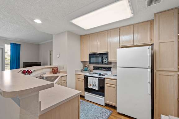 A fully equipped kitchen with a refrigerator, range, microwave, dishwasher and lots of storage cabinets.