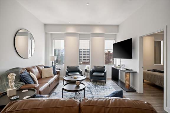 Spacious living room in a furnished short-term rental apartment at Sky on Main with leather seating, accent chairs, contemporary furnishings, and city views.