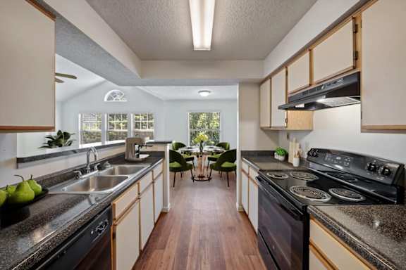 Apartment kitchen with black appliances, double sink, and open dining area at Stonebriar Apartments