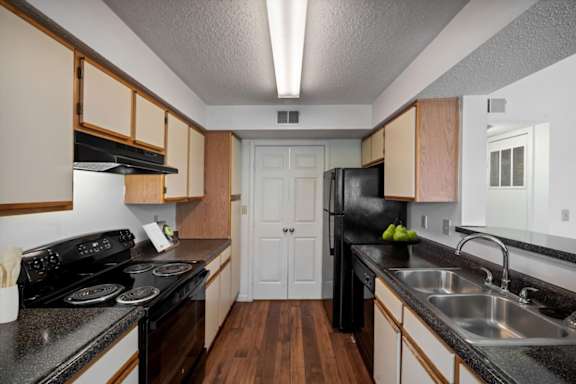 Galley-style kitchen with wood cabinets and black appliances at Stonebriar Apartments Overland Park