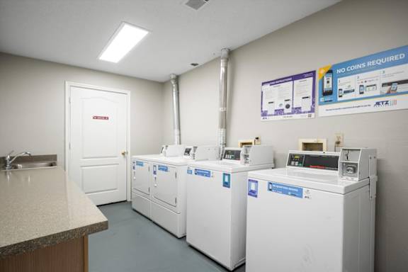 Resident laundry facility at The Claremont Apartments in Overland Park, KS, featuring multiple coinless washers and dryers, folding counters, and bright interior lighting.