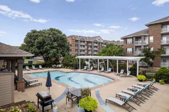 Resort-style outdoor swimming pool at The Claremont Apartments with lounge seating, shaded areas, and surrounding apartment homes in Overland Park, KS.