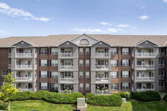 Multi-story apartment building exterior featuring private balconies, landscaped green space, and well-maintained grounds at The Claremont Apartments in Overland Park, KS.
