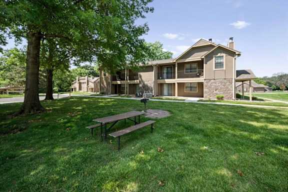 A picnic table and BBQ grill under a tree, with an apartment building at Waterford Place Apartments & Townhomes in the background
