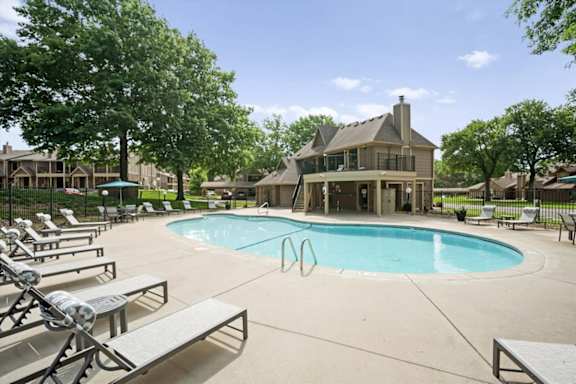 A large outdoor swimming pool surrounded by sun loungers and trees.