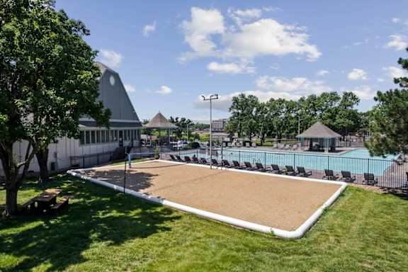 Sand volleyball court adjacent to the swimming pool and clubhouse amenities at Wind River Lodge Apartments in Lenexa, Kansas.