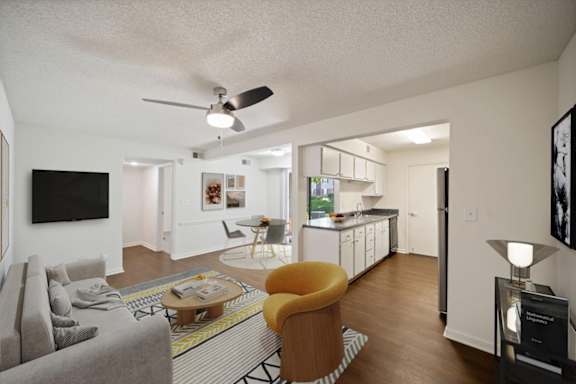 Open-concept living room featuring modern furnishings, wood-style flooring, and direct access to the kitchen and dining areas.