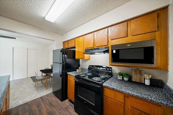 Apartment kitchen with wood cabinetry, black appliances, updated countertops, and adjacent dining area.