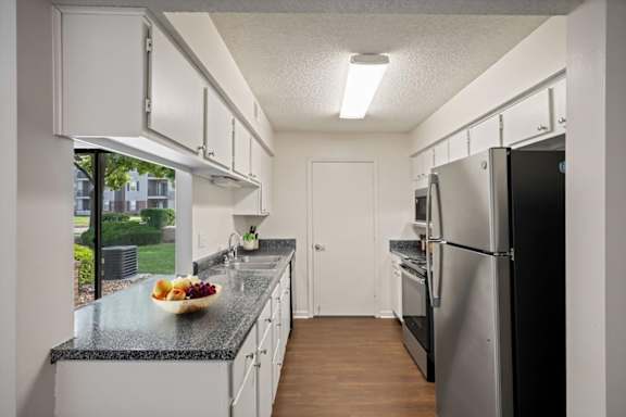 Bright kitchen featuring white cabinetry, modern appliances, generous countertop space, and a large window overlooking the community.