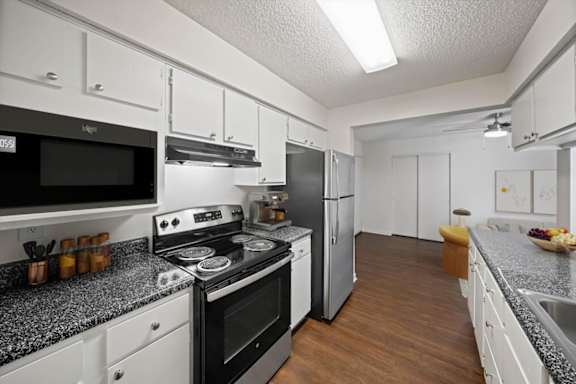 Updated kitchen with stainless steel appliances, white cabinetry, and an open floor plan connecting to the living area.