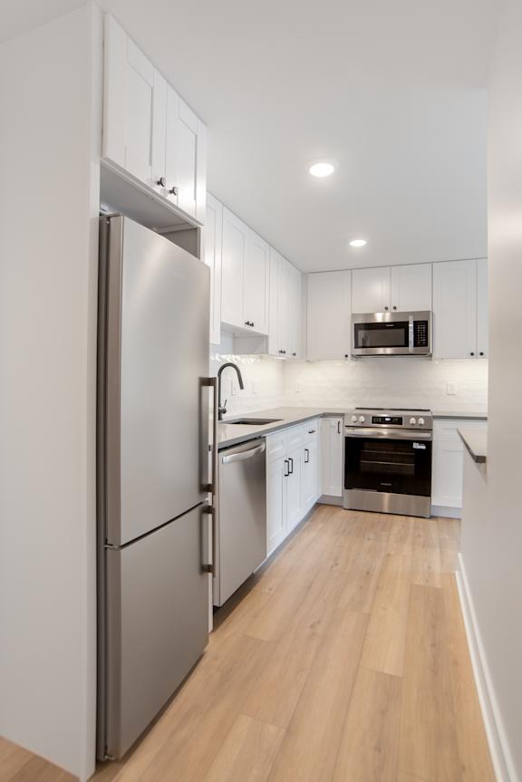 A modern kitchen with a stainless steel refrigerator and wooden flooring.