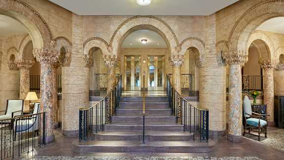 A grand staircase with arched columns and a chandelier hangs in the center of a spacious hall.