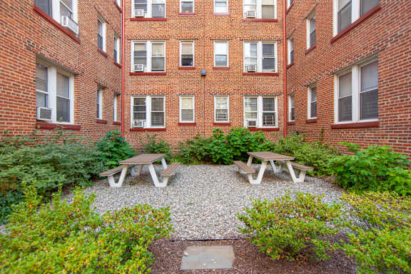 A courtyard with picnic tables and bushes in front of a brick building.