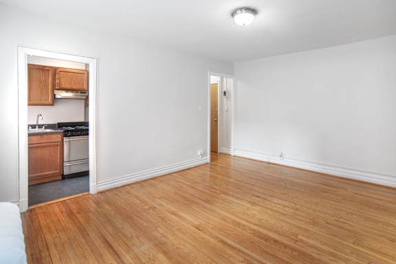 an empty living room with wood flooring and a kitchen