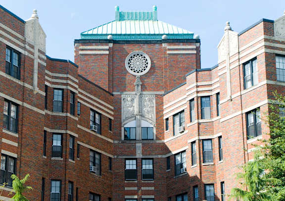 A large red brick building with a green roof and a large white statue in the middle.