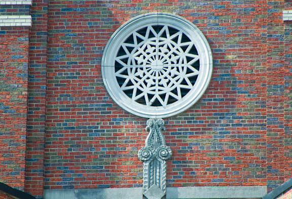 A circular window with a geometric pattern is set in a brick wall.