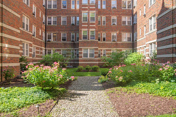 A courtyard with a gravel path and flower beds in front of a brick building.