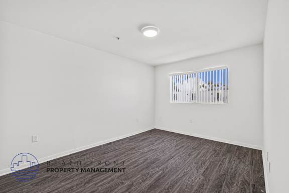 a bedroom with white walls and wood flooring and a window